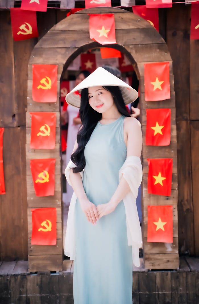 digital Woman in traditional Vietnamese attire with conical hat in front of archway adorned with flags.